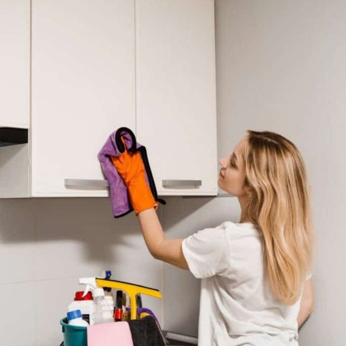 Professional cleaning service for general house cleaning. Housewife cleans the kitchen from dirt and dust. Cleaning woman is wiping kitchen with microfiber rag